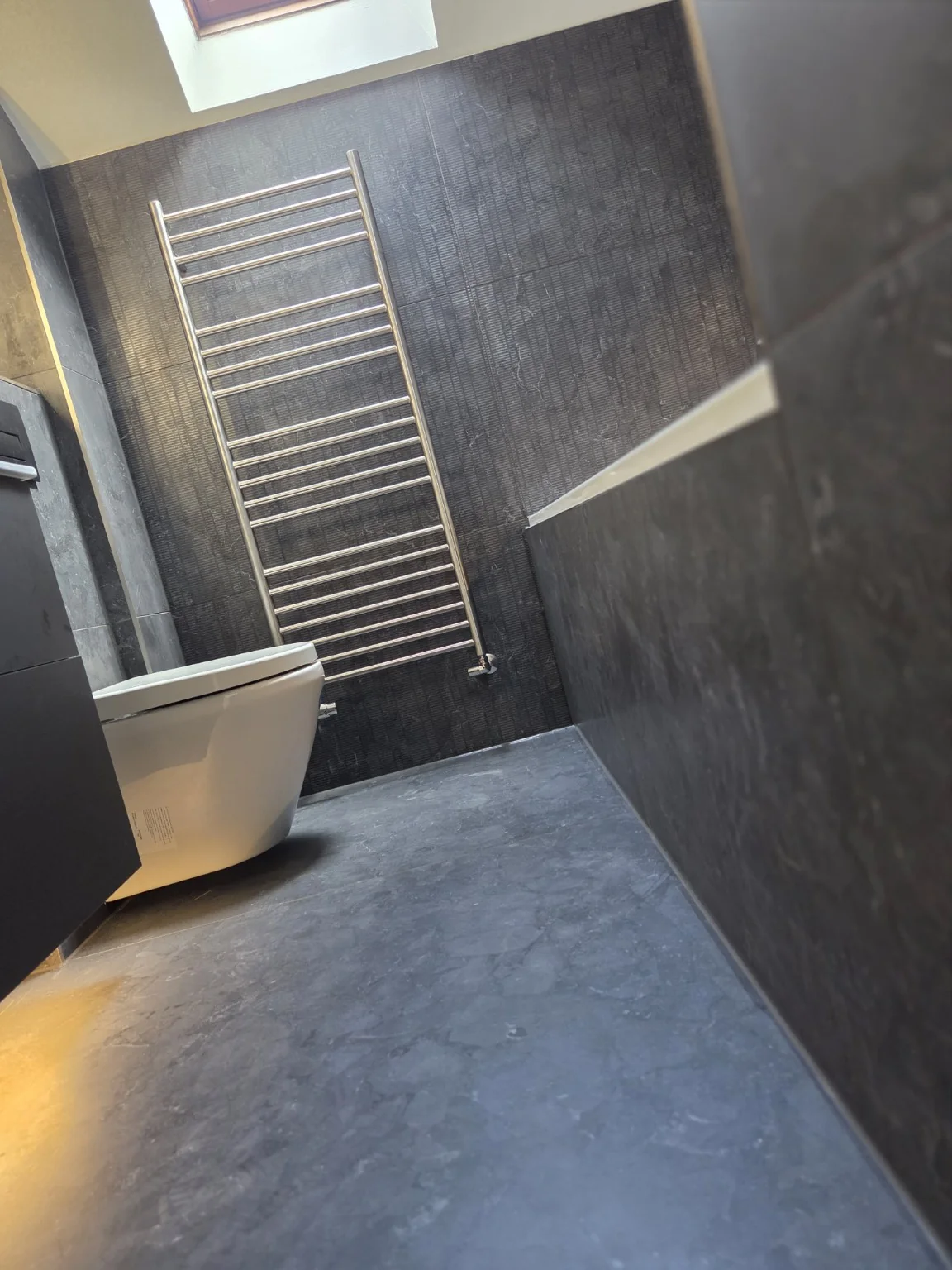 Chrome towel radiator against textured charcoal tiles