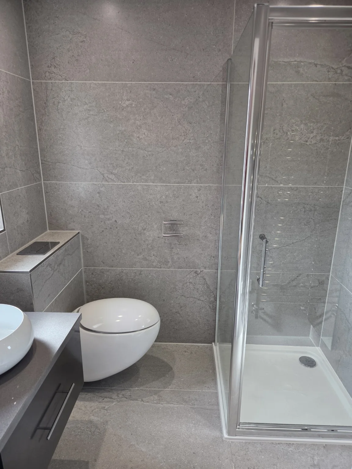 Grey stone shower room with wall-hung WC and glass enclosure
