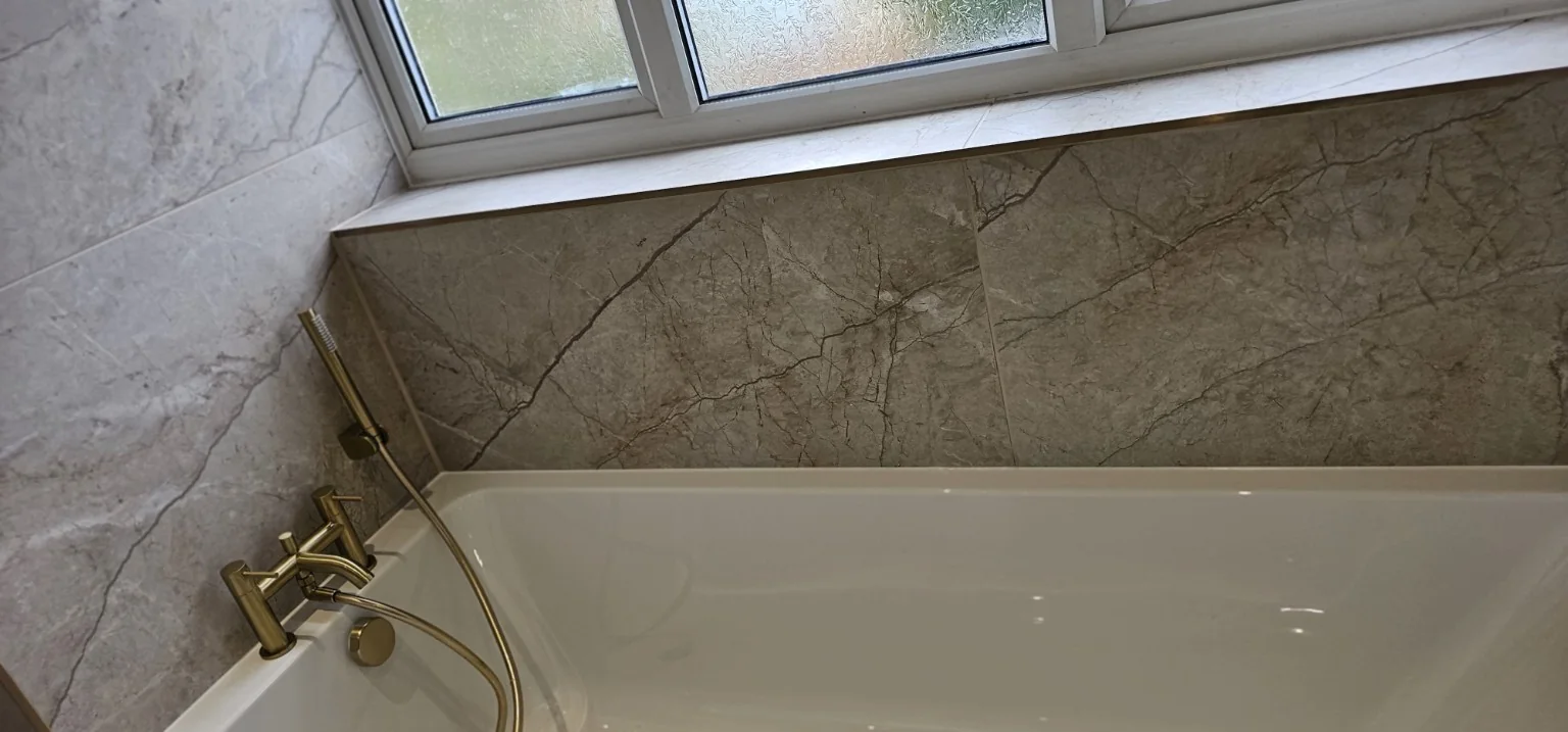 Bath with stone-effect tiling and brushed gold fittings