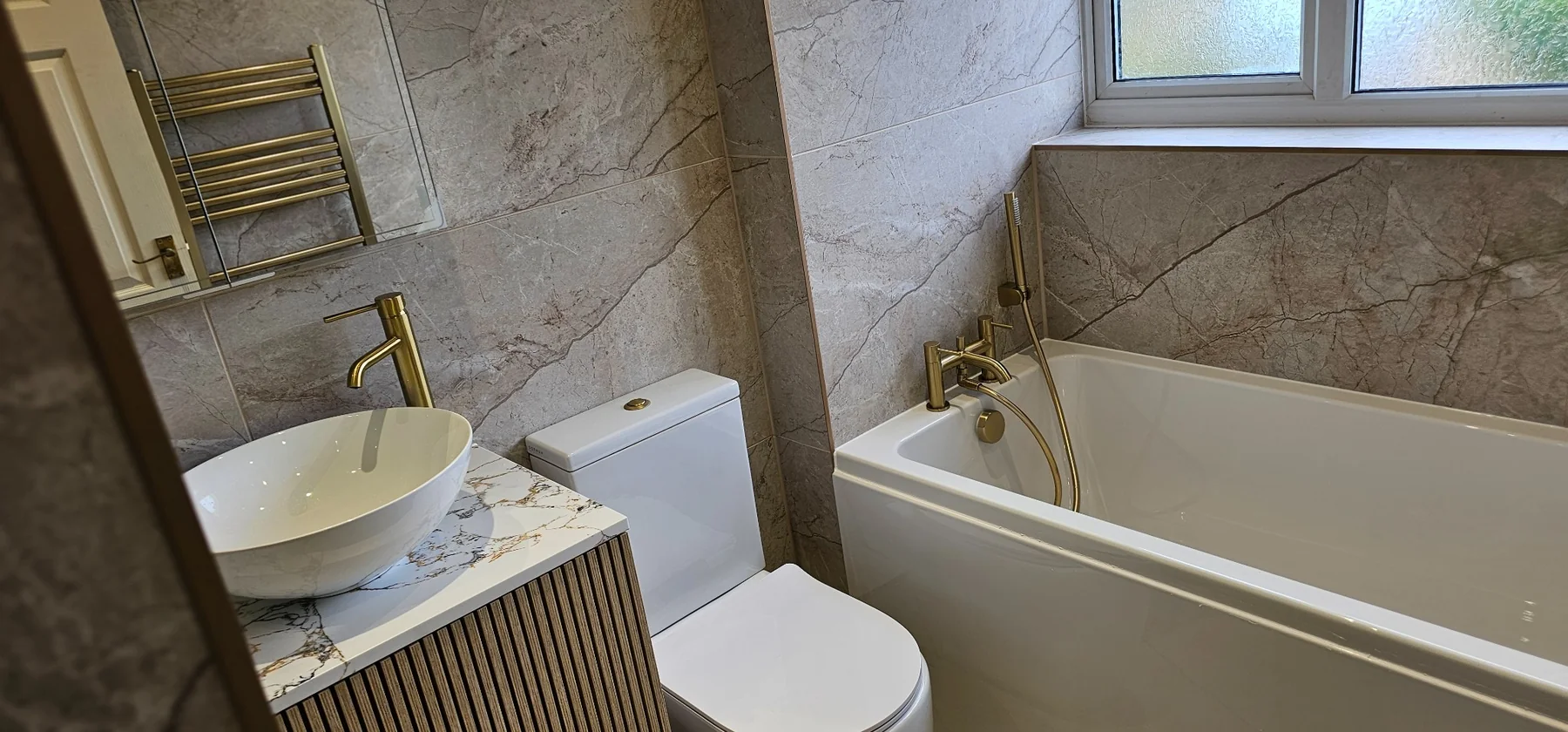 Stone and gold bathroom with fluted vanity, toilet and bath